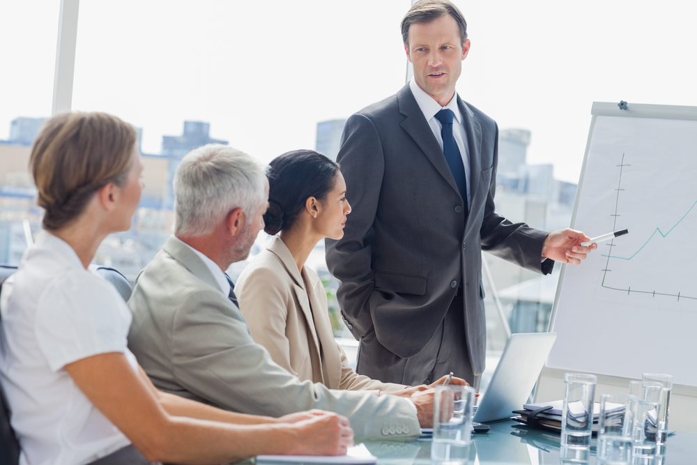 Businessman pointing at whiteboard during a meeting in front of attentive colleagues